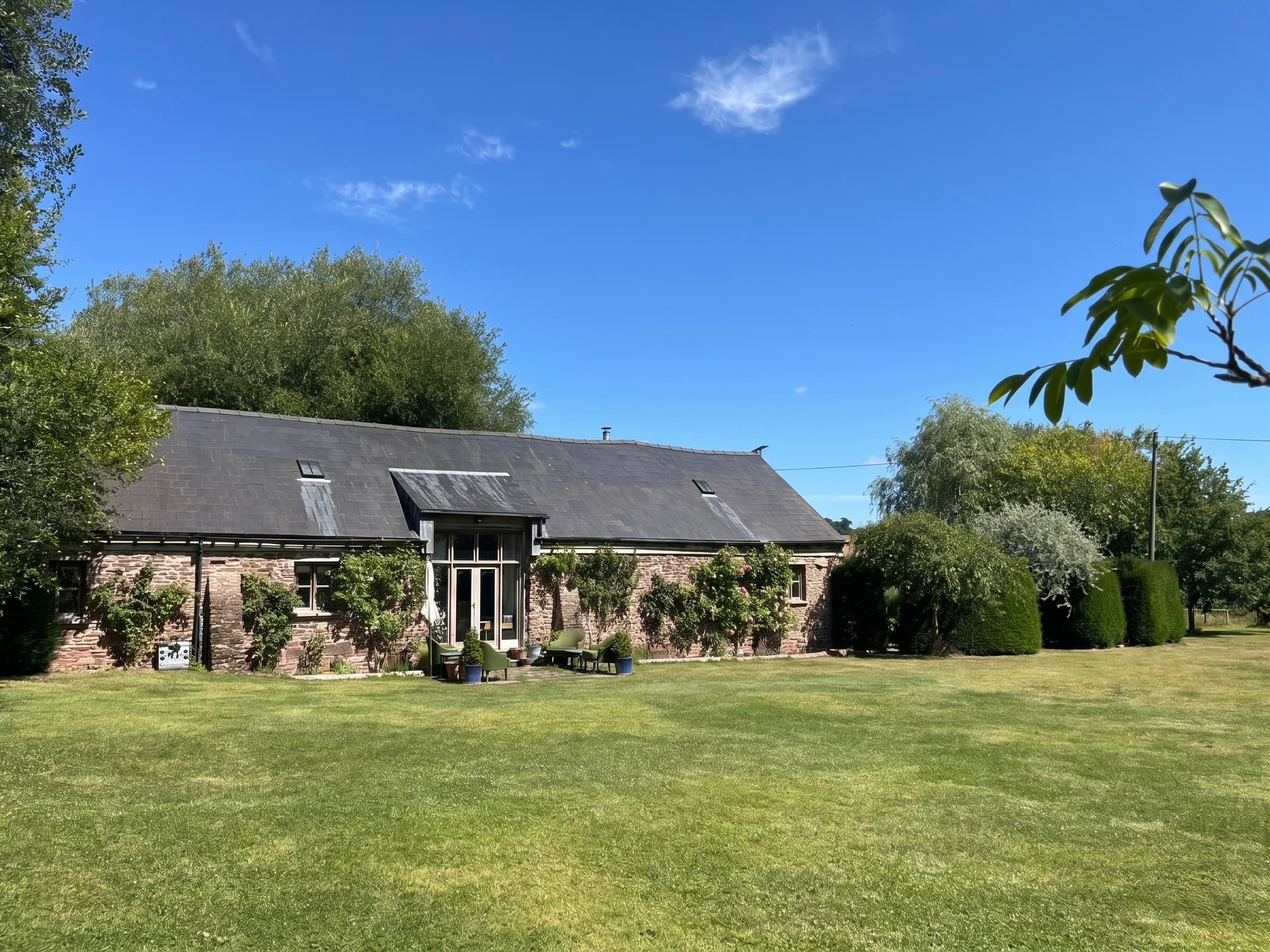 Ruthlin cottage from across the lawn — stone frontage, climbing plants and open countryside in summer