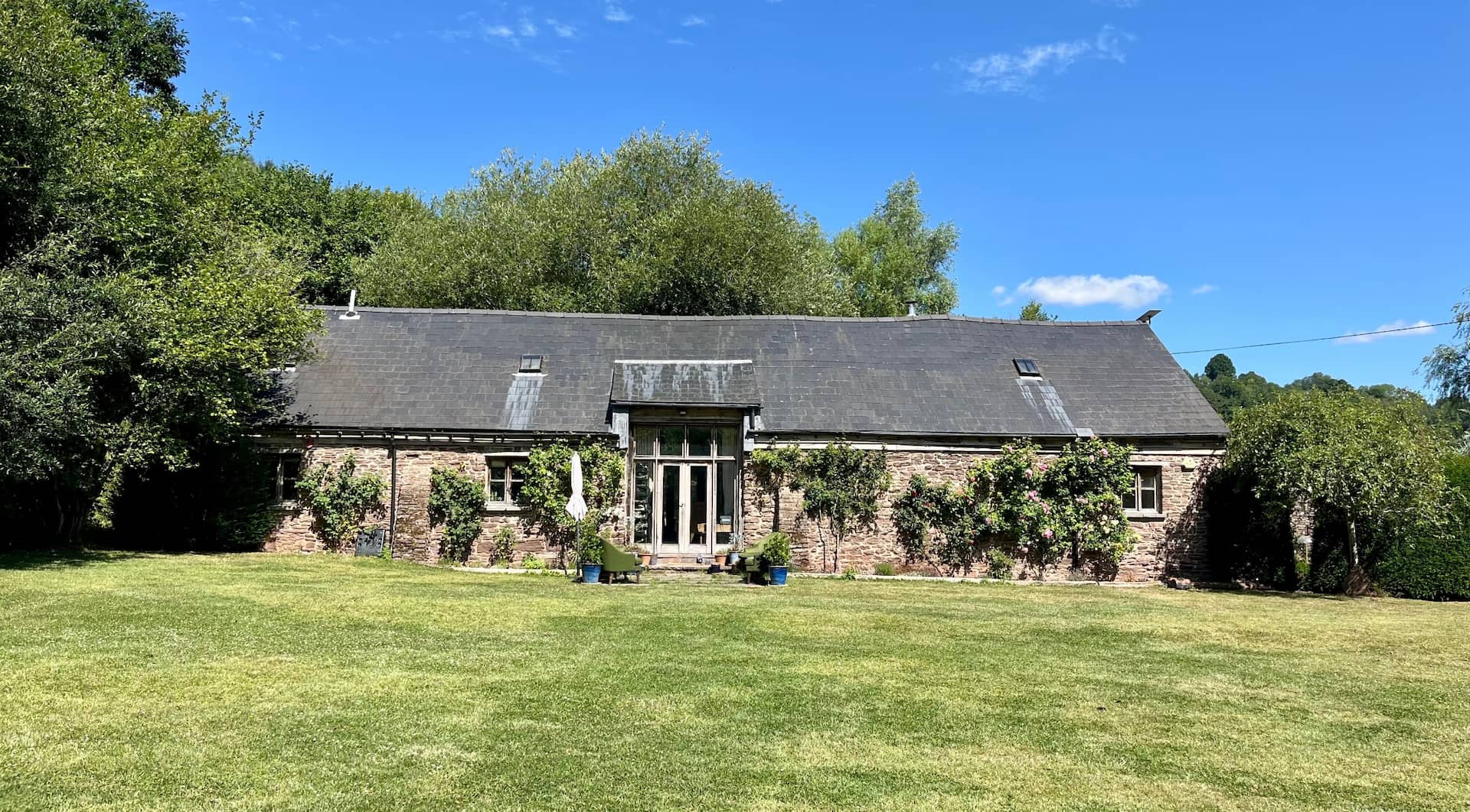 The converted stone barn at Ruthlin, a family-run holiday let near Monmouth, with roses on the walls, seen across the lawn