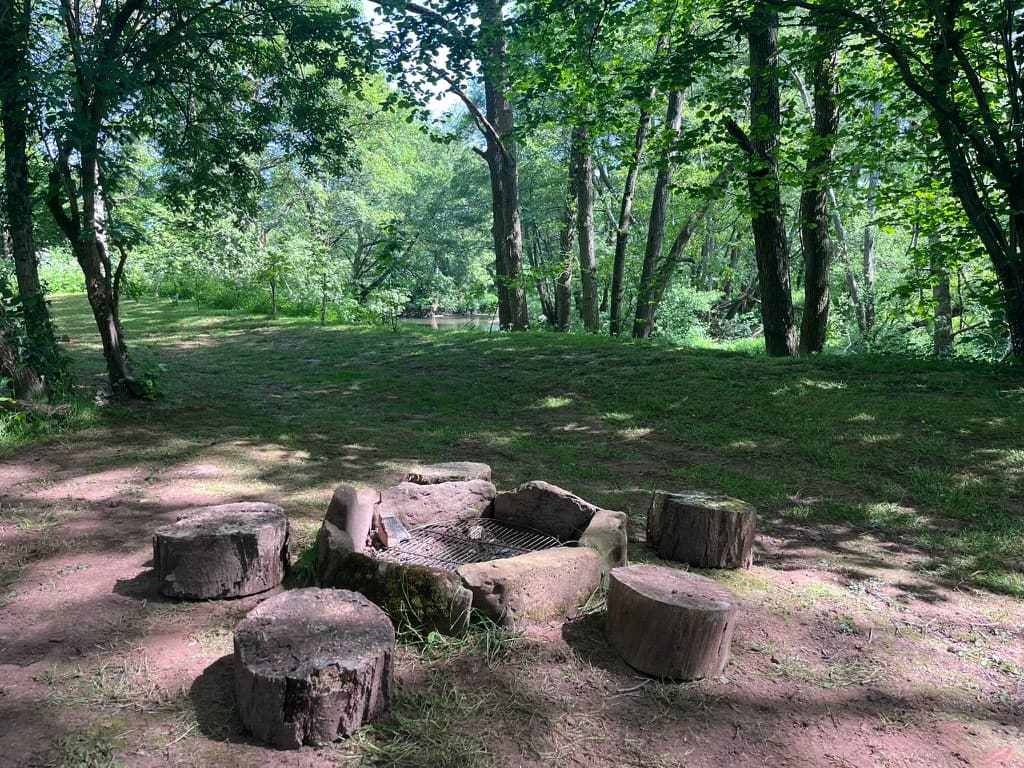 A riverside firepit ringed with log seats in the woodland at Ruthlin, a riverside retreat in Monmouthshire
